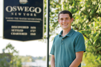 Tom Drumm '15 stands in front of an Oswego, New York sign. Tom represents Oswego in the County Legislature.